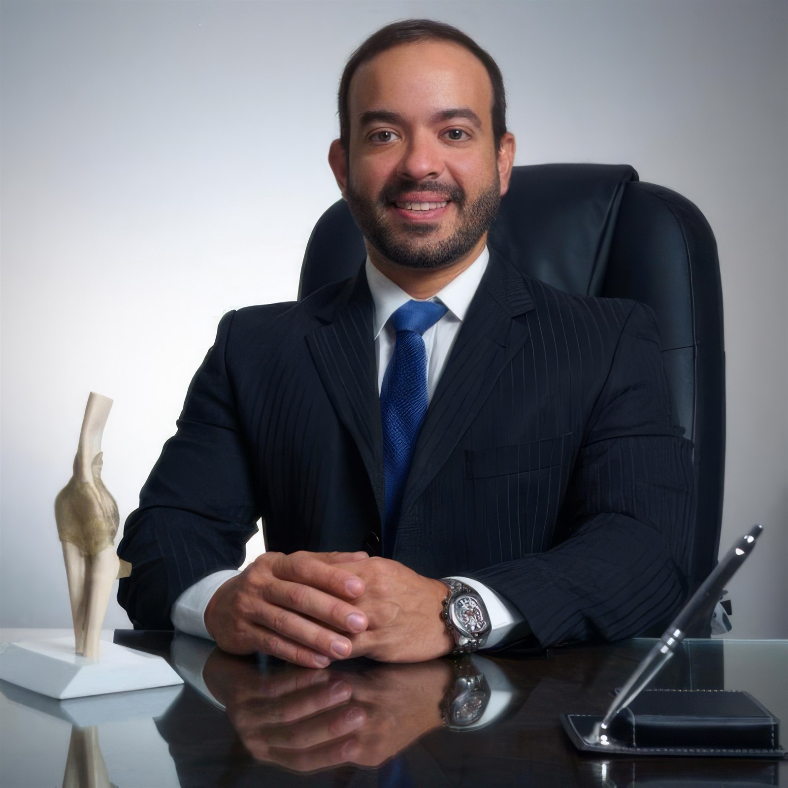 Dr. José Inácio sentado em seu consultório, ao lado de um modelo anatômico de joelho